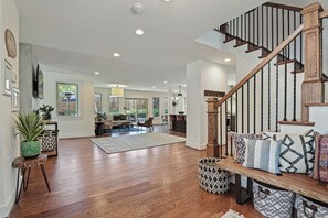 A spacious living area with hardwood flooring, a wooden staircase, and a view of the backyard through large windows. - The Crestwood House - Family Friendly Retreat with Private Backyard - DCA  (Alexandria)