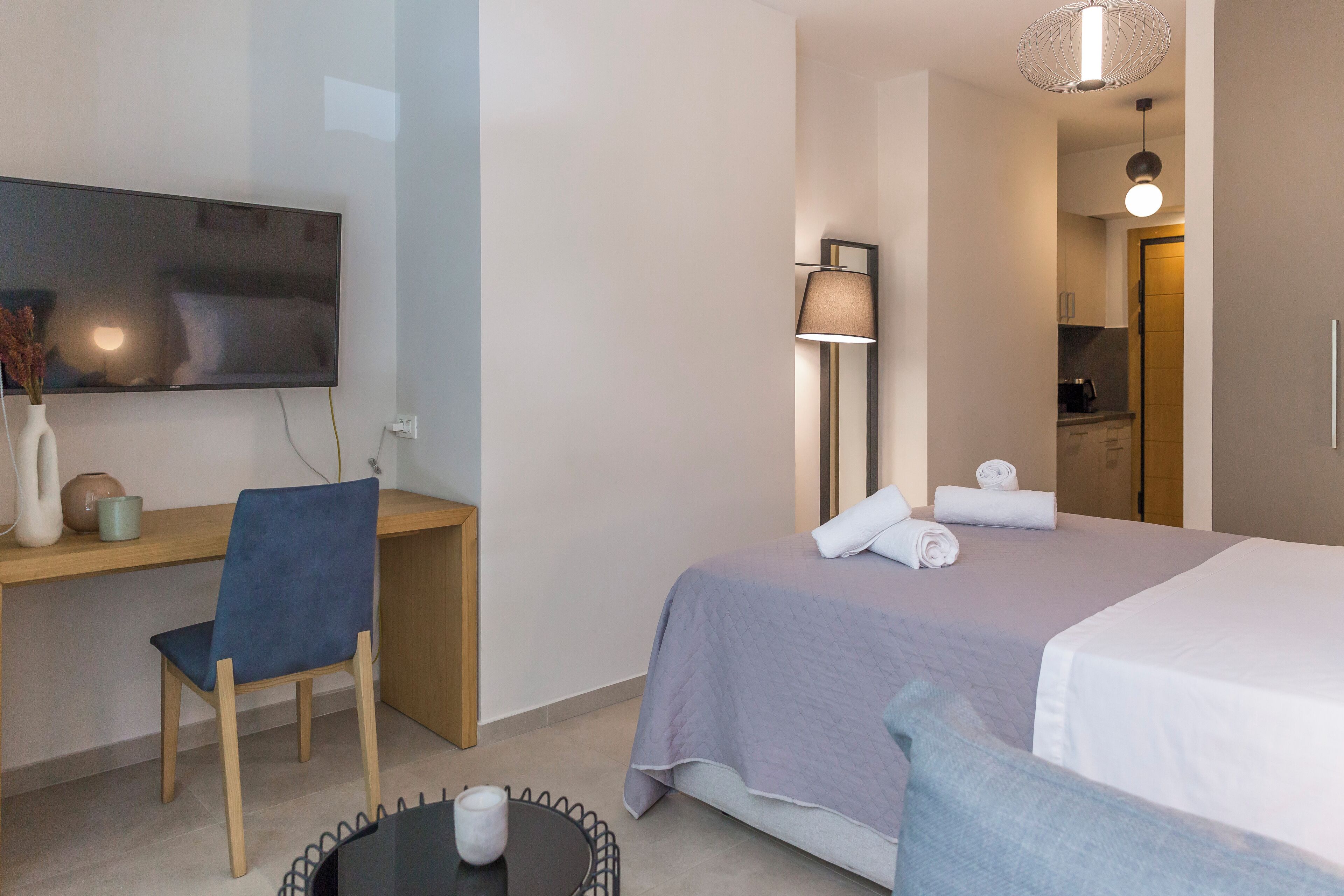 A hotel room with a bed, a desk, a chair, a TV, and a lamp.
