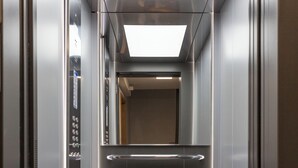 A modern elevator with a metallic interior, a handrail, and a control panel on the left. - Cubes Living Athens, Studio 302 (Athina)