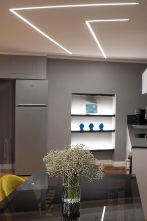 Una cocina moderna con refrigerador empotrado, un estante blanco con adornos, y un jarrón con flores sobre la mesa de comedor.