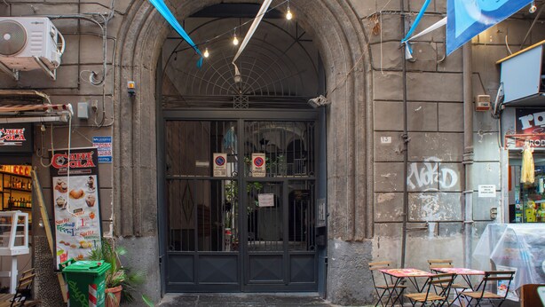 A café with a dark entrance, outdoor seating, and a sign advertising a coffee drink. - New apartment in the historic center of Naples, for families or couples.  (Napoli)