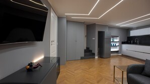 A modern kitchen with a built-in oven, a refrigerator, and a microwave. There is a wooden herringbone floor and a gray sofa in the living area. - New apartment in the historic center of Naples, for families or couples.  (Napoli)