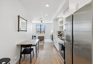 A modern kitchen with a stainless steel refrigerator, wooden dining table, and chairs.