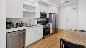 A modern kitchen with white cabinetry, stainless steel appliances, and a wooden dining table.
