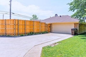 Un garaje residencial con cerco de madera, camino de concreto y césped.