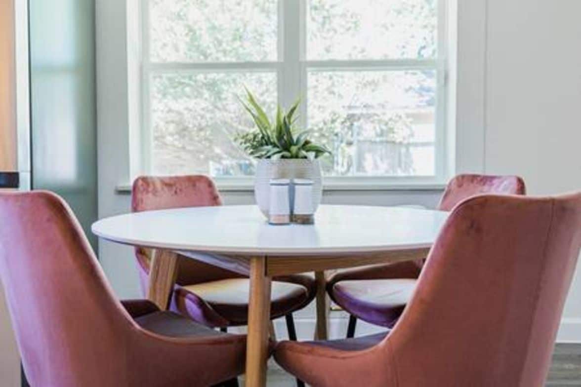 A round table with four chairs, a potted plant, and a window with a view of greenery.