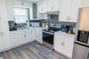 A modern kitchen with white cabinets, a microwave, an oven, and a refrigerator.