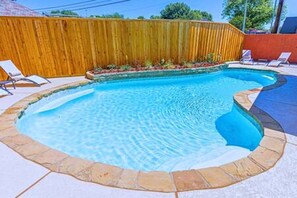 Une piscine entourée d’une clôture en bois, avec des chaises longues et une terrasse carrelée.