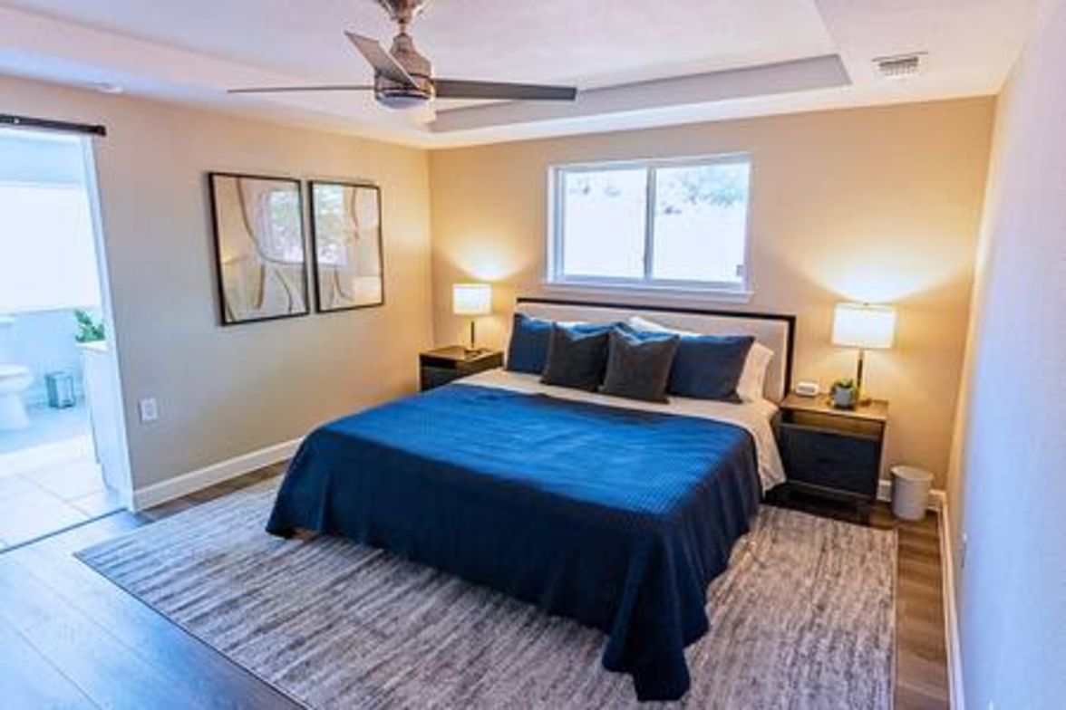 A bedroom with a bed, two bedside tables, a ceiling fan, a window, and a door.