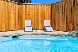 Una piscina con dos sillas de descanso y una valla de madera.
