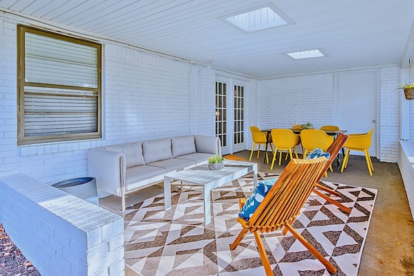 Una habitación con pared de ladrillo blanco, un sofá, una mesita de centro, sillas amarillas y una alfombra estampada.