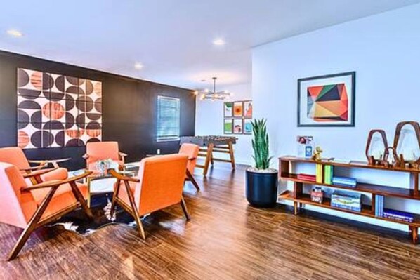 Una sala de estar moderna con piso de madera, sillones naranjas, una estantería y un cuadro abstracto grande en la pared.