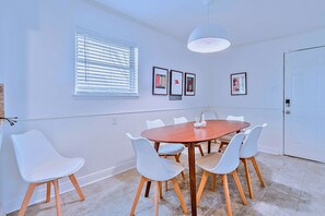A dining area with a round wooden table, six white chairs, and a ceiling light fixture.