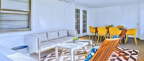 Una habitación con pared de ladrillo blanco, un sofá, una mesa de centro, un tapete estampado y sillas amarillas.