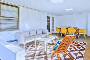 Una habitación con pared de ladrillo blanco, un sofá, una mesa de centro, un tapete estampado y sillas amarillas.