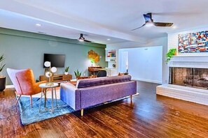 A modern living room with a sofa, armchair, and coffee table, a fireplace, and a flat-screen TV mounted on the wall. - Location + Monthly + WiFi + Desk + Pet (Grand Prairie)