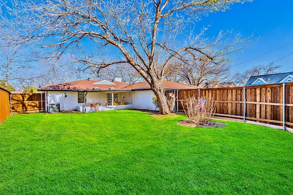 A residential backyard with a well-maintained lawn, a wooden fence, and a house with a red roof.