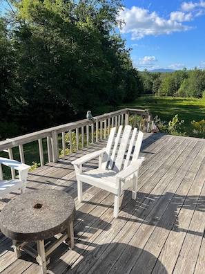 Una terraza de madera con una silla Adirondack blanca y una mesa de piedra.