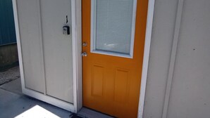 Une porte orange fermée, dotée d’un cadre blanc et d’une fenêtre avec des stores horizontaux.