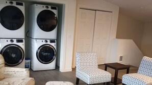 Une buanderie avec des machines à laver superposées, une porte blanche et des chaises à motifs.