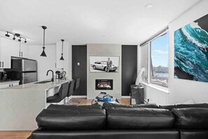 A modern kitchen with a central island, a dining area with a black leather couch, and a large window with a city view. - Modern & Comfy in Downtown ~ Views ~ Pool (Vancouver)