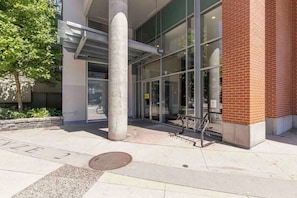 A modern building entrance with glass doors, a metal bench, and a concrete pillar. - Modern & Comfy in Downtown ~ Views ~ Pool (Vancouver)