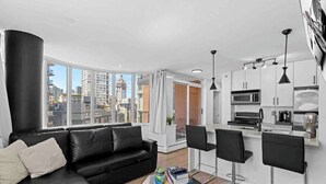 A modern living room with a black leather sofa, a glass coffee table, and a city view through large windows. - Modern & Comfy in Downtown ~ Views ~ Pool (Vancouver)
