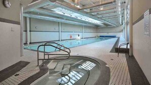 An indoor swimming pool with a diving board, a changing room, and a ceiling with visible ductwork. - Modern & Comfy in Downtown ~ Views ~ Pool (Vancouver)