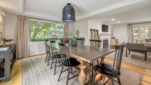 Un espace repas avec une grande table en bois, des chaises noires et un luminaire suspendu.
