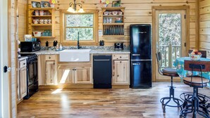 Une cuisine rustique, située dans une cabane en bois, avec un poêle en bois, un réfrigérateur noir et un coin repas comprenant une table et des chaises.