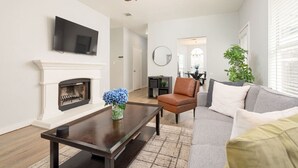 A living room with a fireplace, a television mounted on the wall, a ceiling fan, and a dining area in the background. - Super Clean/ Fun Environment! Low Cleaning Fee! (Georgetown)