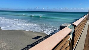 Une promenade en bois qui mène à une plage où l’eau est d’un bleu turquoise limpide et où les vagues sont douces.