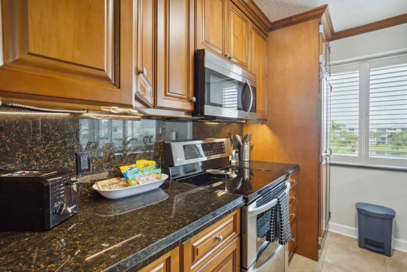 A kitchen with wooden cabinets, a microwave, a toaster, and a trash bin.