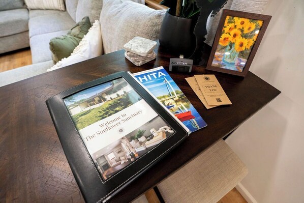 A tablet displaying a welcome message for The Sunflower Sanctuary, a brochure, a framed picture of sunflowers, and a thank you card on a wooden table. - Fire Pit, Fully Stocked, Family-Friendly Oasis (Wichita)