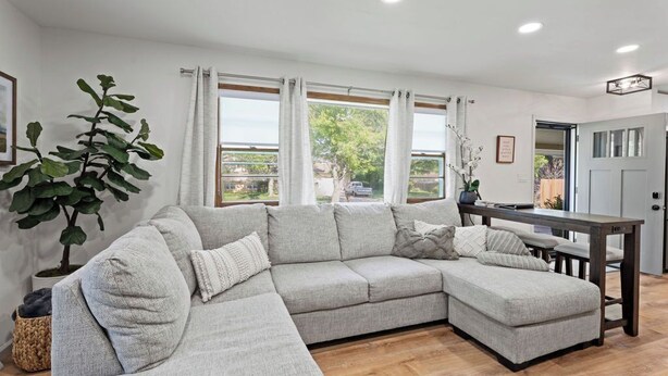 A modern living room with a sectional sofa, a dining table, and a large window with curtains. - Fire Pit, Fully Stocked, Family-Friendly Oasis (Wichita)