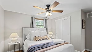 A bedroom with a bed, two bedside tables, a ceiling fan, a window with curtains, and a door. - Fire Pit, Fully Stocked, Family-Friendly Oasis (Wichita)