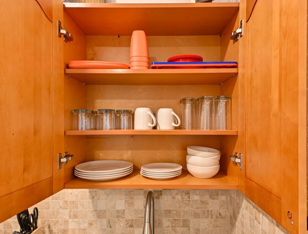 A kitchen with wooden cabinets, a tiled backsplash, and shelves holding plates, cups, and jars.
