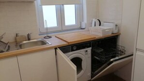 Een kleine keuken met een wasmachine, een spoelbak en een raam met zonwering.