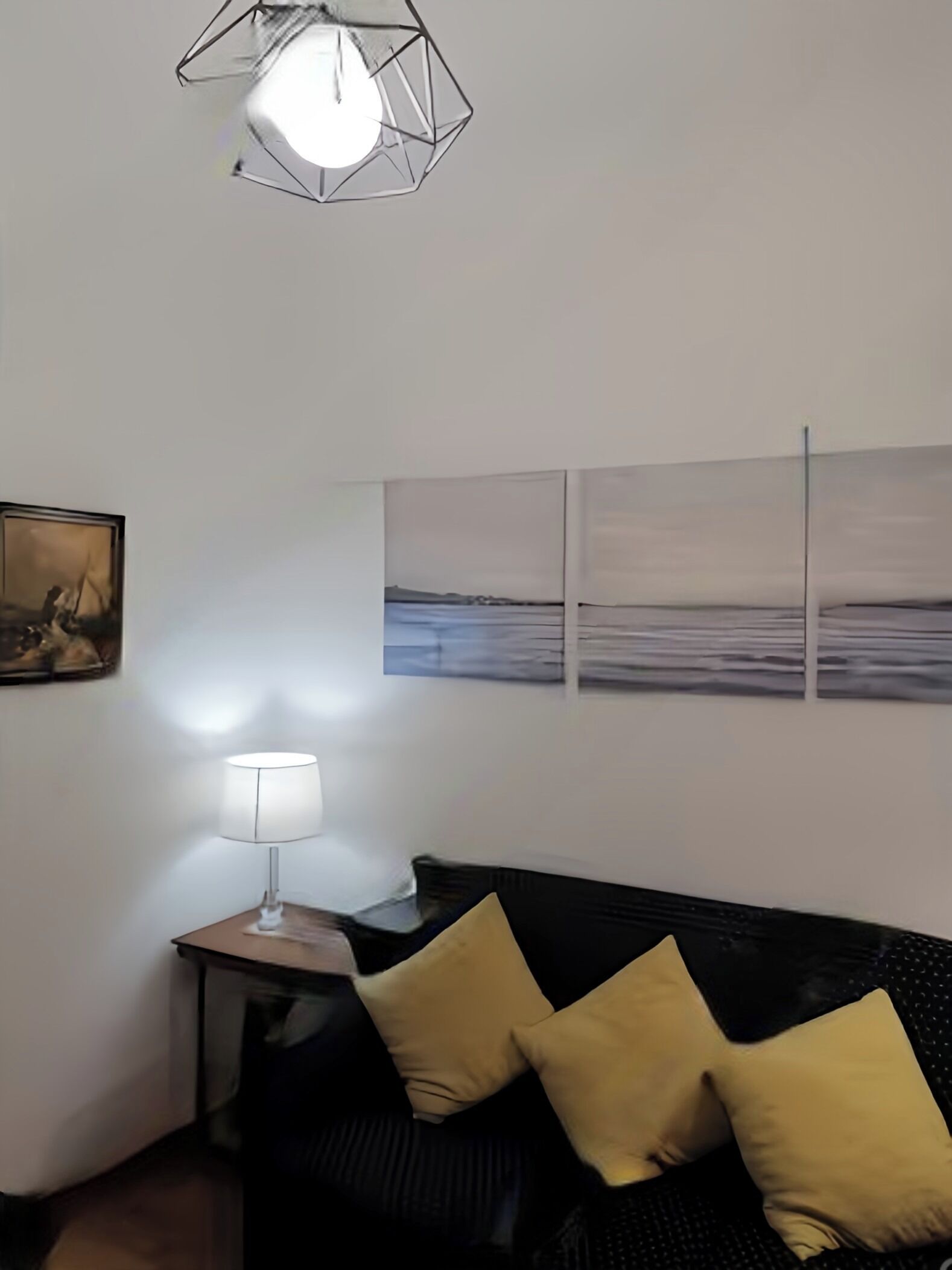 A room with a black sofa, a small table with a lamp, and three framed pictures on the wall.