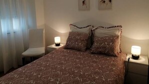 Een slaapkamer met een bed met een geruit sprei, twee kussens, een nachtkastje met een lamp en twee aan de muur hangende foto’s van herten.