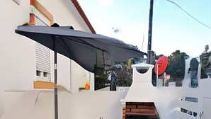 Een terras met een tafel en stoelen, een geplaveid vloertje, een schoorsteen en een gele parasol.