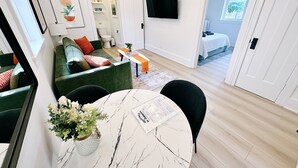 Moderni olohuone, jossa on vihreä sohva, valkoinen sohvapöytä ja seinälle asennettu televisio.