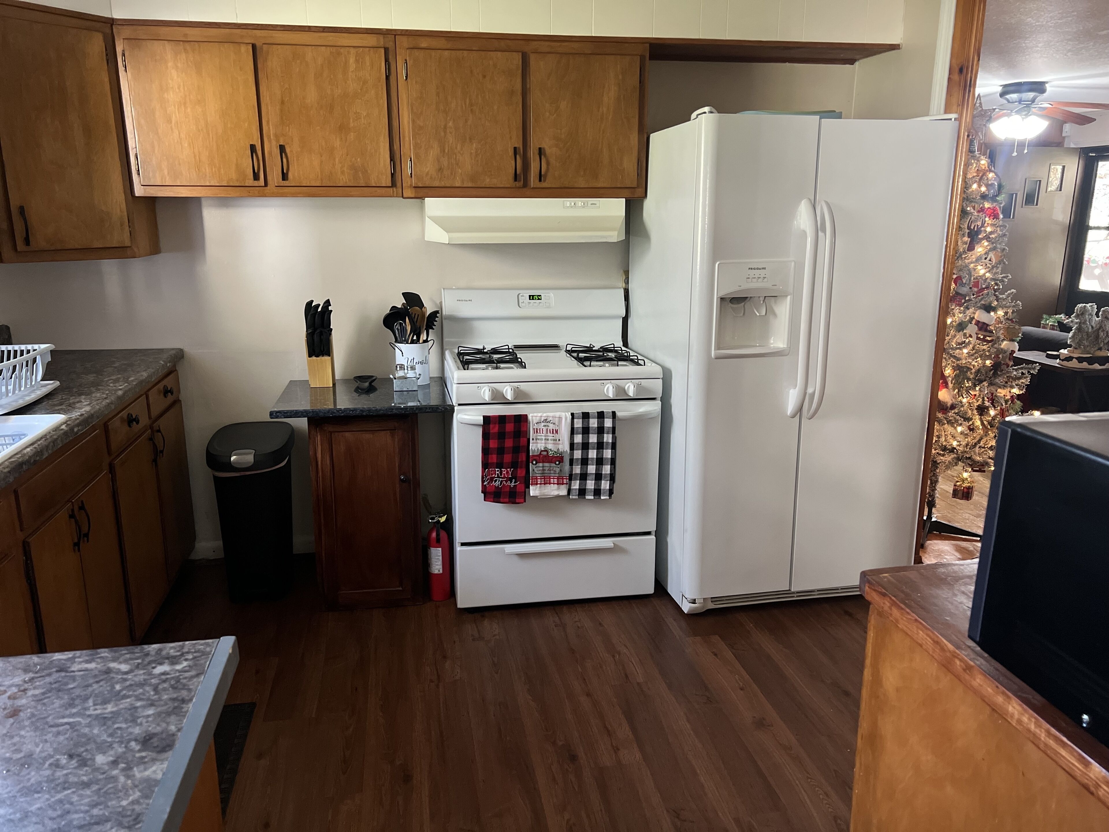 A kitchen with wooden cabinets, a white stove, a refrigerator, and a small trash bin.