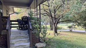 A covered porch with a wooden chair, a brick wall, and a large tree in the background. - Dragons Lair - motorcycle friendly, all paved roads, lockable garage, no incline (Robbinsville)