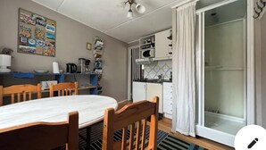 Une cuisine compacte équipée d’un four à micro-ondes, d’une machine à café et de placards. On y trouve une table à manger avec des chaises et un tapis à motifs.