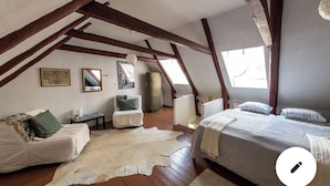 Une chambre avec un plafond en pente, des poutres en bois, un lit, une chaise, un tapis et une fenêtre.