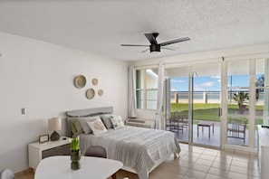 A bedroom with a bed, bedside table, lamp, and a view of the outdoors through a sliding glass door.