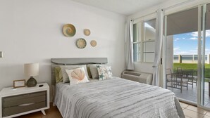 A bedroom with a bed, nightstand, and a view of the outdoors through a sliding glass door. - Beachfront Petite Paradise unit at Pelican Reef 103 (Rincon)