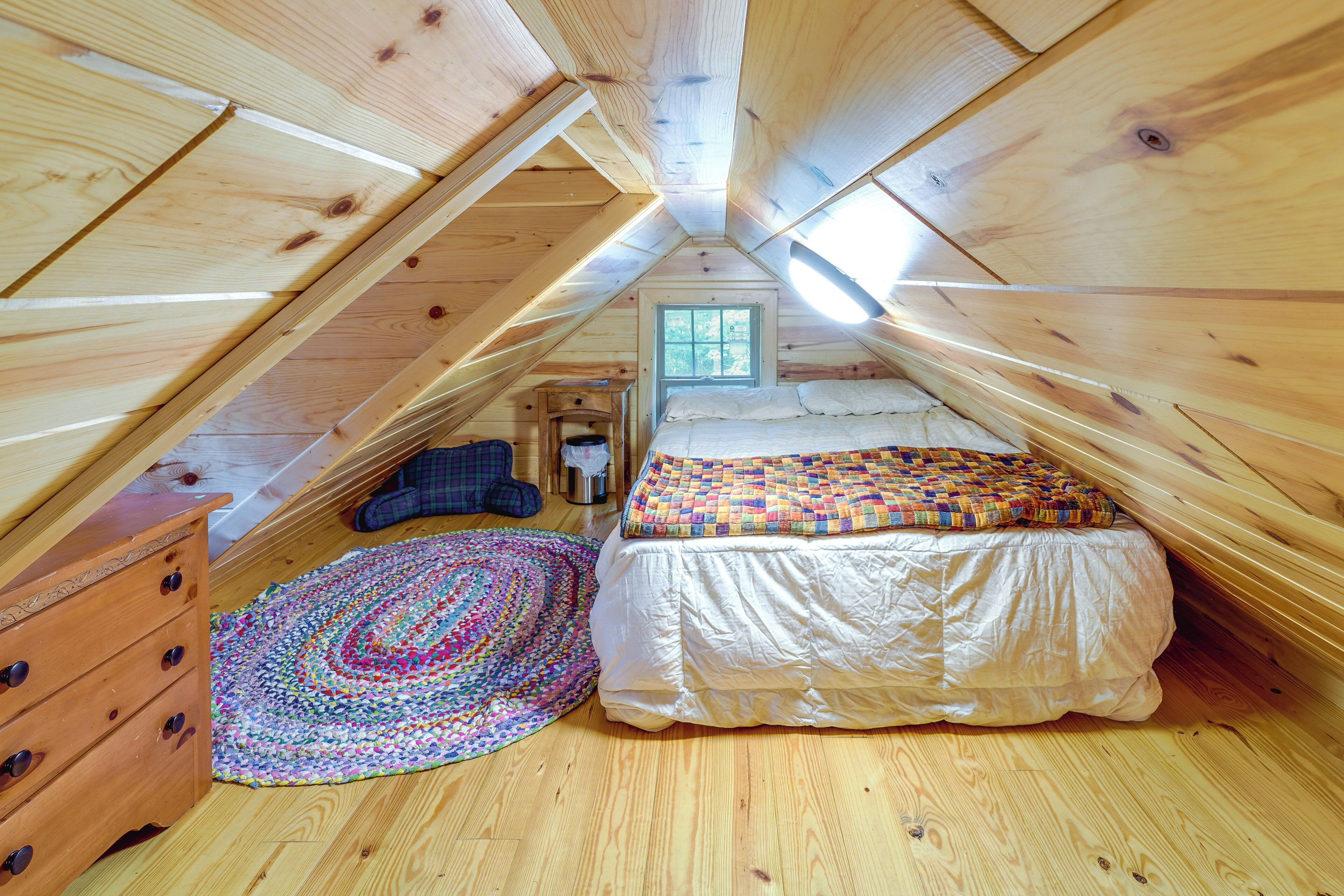 A cozy attic bedroom with a wooden ceiling, a bed with a colorful quilt, a wooden dresser, and a patterned rug.