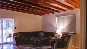 Una sala de estar con un sofá seccional marrón oscuro, una mesita redonda con lámpara, un sillón reclinable y una ventana con persianas.